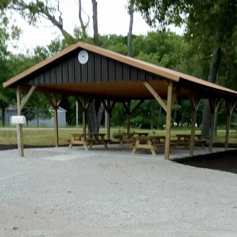 Wooden picnic pavilion with benches in park setting.